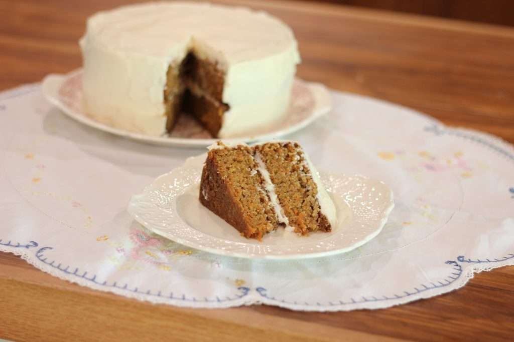 A slice of carrot cake on plate with carrot cake in background