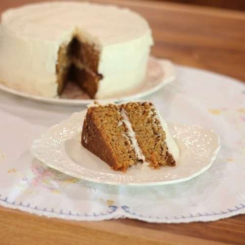 A slice of carrot cake on plate with carrot cake in background