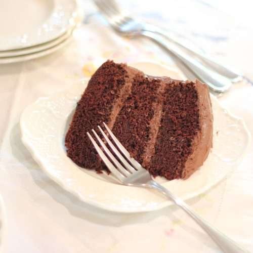 Slice of 3 layer chocolate cake on plate with fork