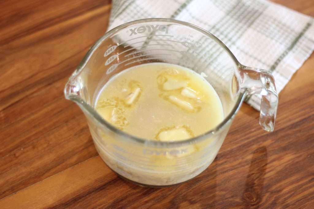 Measuring cup with oats, butter, and honey soaking in hot water.