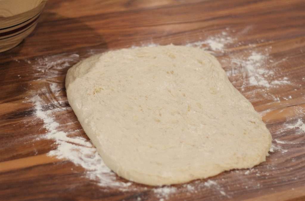 Bread dough stretched out to rectangle shape on counter.