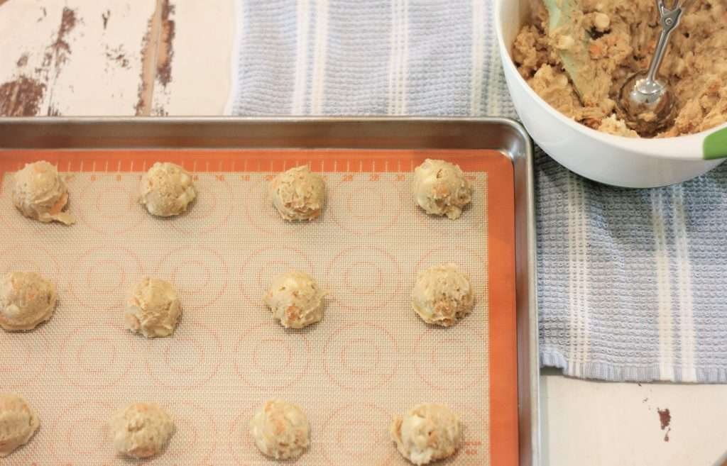 Baking sheet with cookie dough balls on it with mixing bowl to the side.