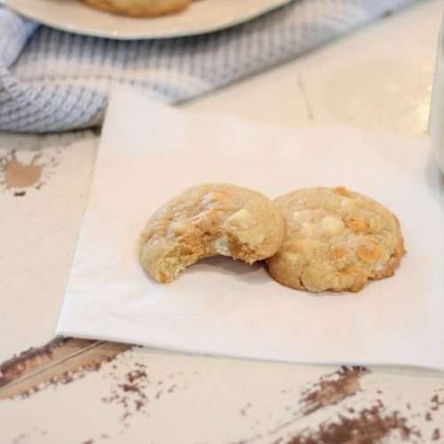 two cookies on a napkin with a glass of milk. One cookie has a bite out of it.