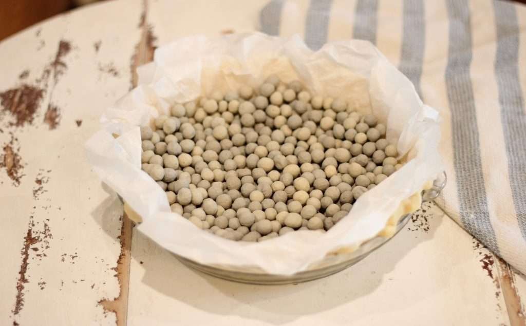 Uncooked pie crust with pie weights on parchment paper