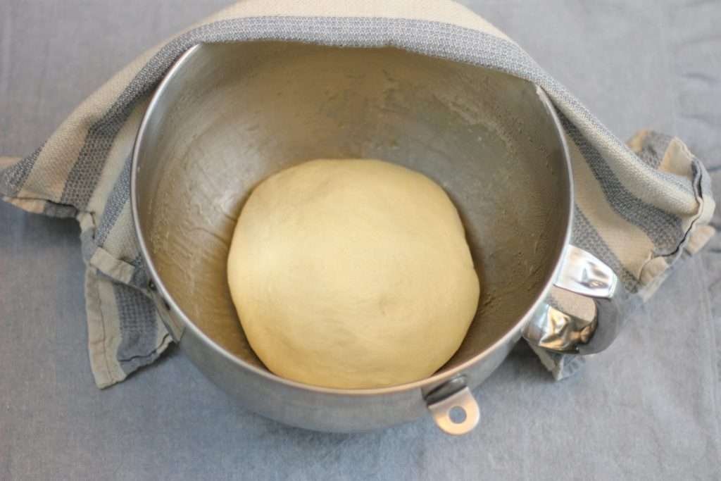 Bread dough in metal mixing bowl set to rise.