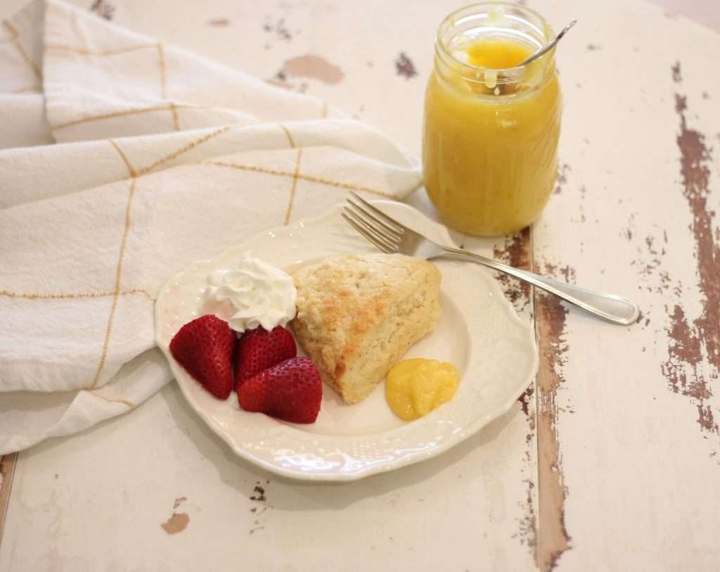 Eggnog Scottish Scone on white plate with strawberries, whipped cream, and lemon curd on the side. 