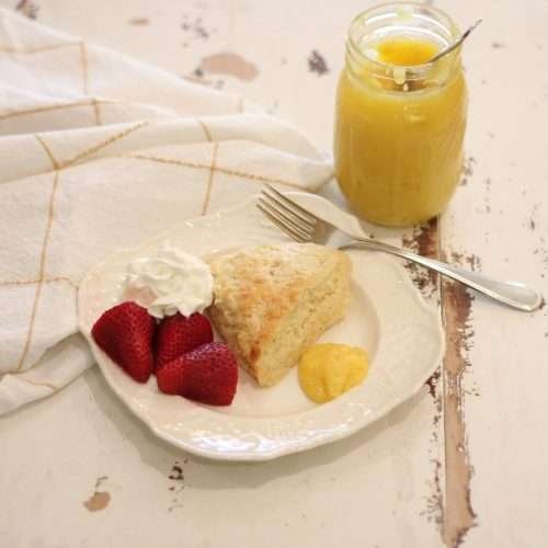 Eggnog Scottish Scone on white plate with strawberries, whipped cream, and lemon curd on the side.