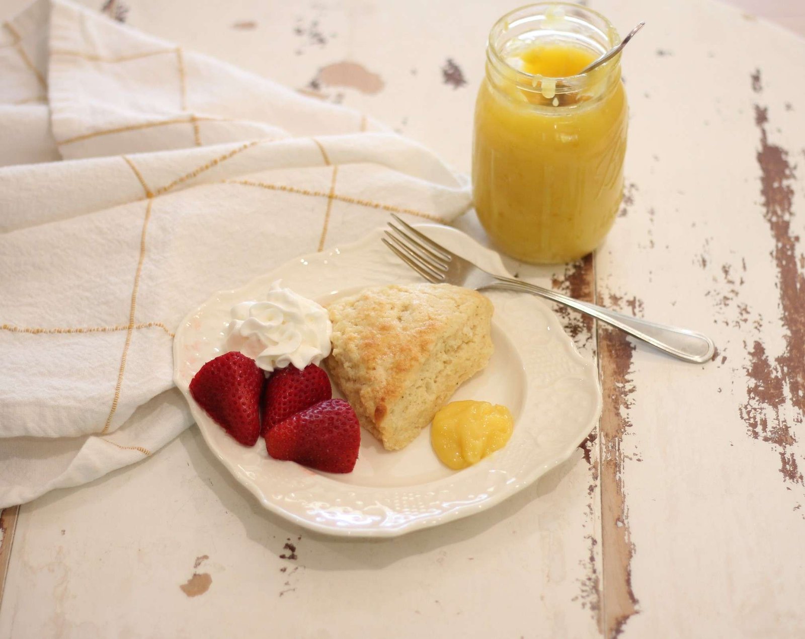 Eggnog Scottish Scone on white plate with strawberries, whipped cream, and lemon curd on the side.