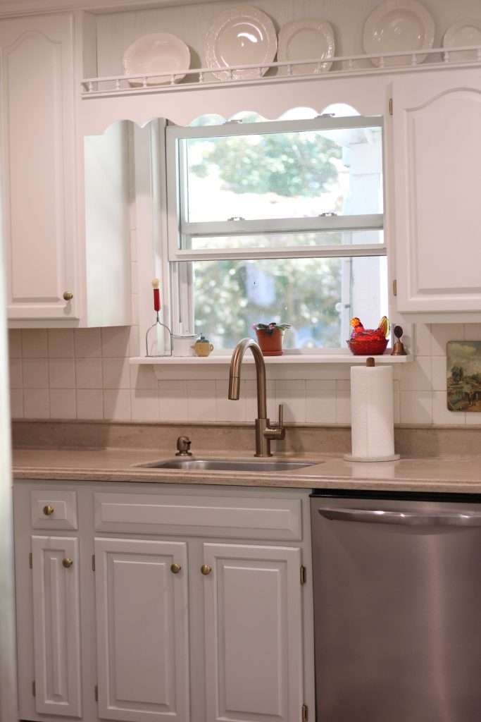 Kitchen sink looking out window with Painted kitchen cabinets.