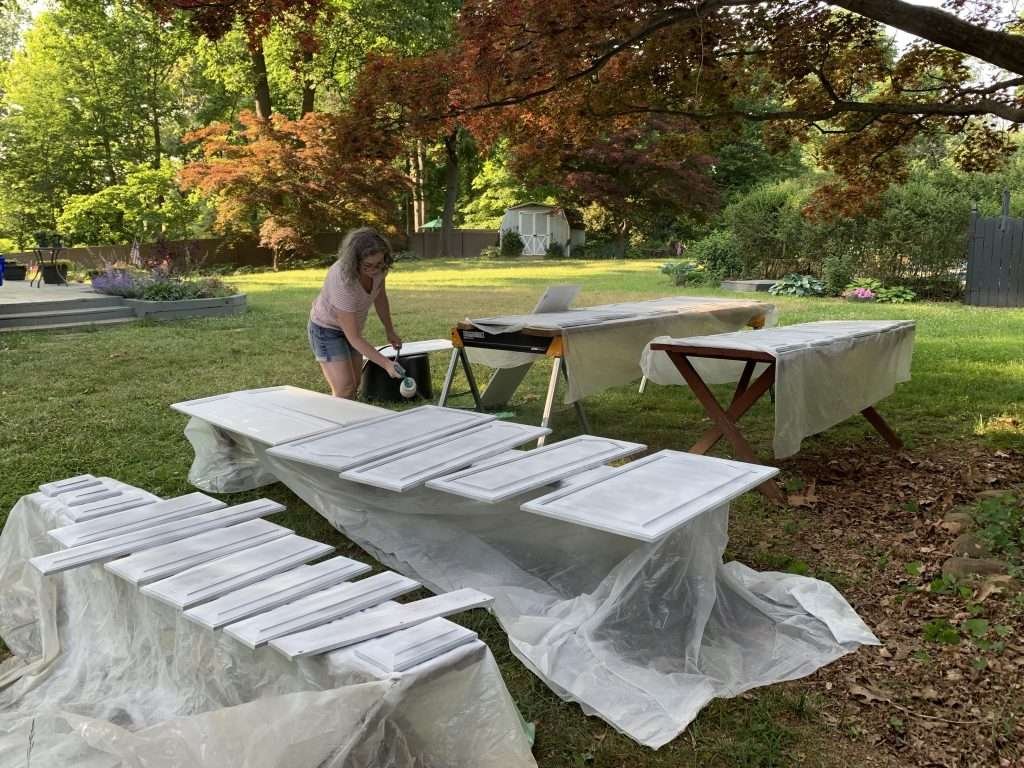 woman painting kitchen cabinet doors outside with a spray gun and primer. 