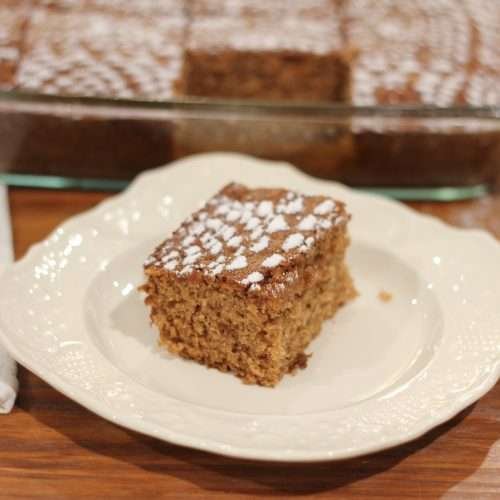 A slice of Applesauce Spice Cake on white plate with cake behind it.