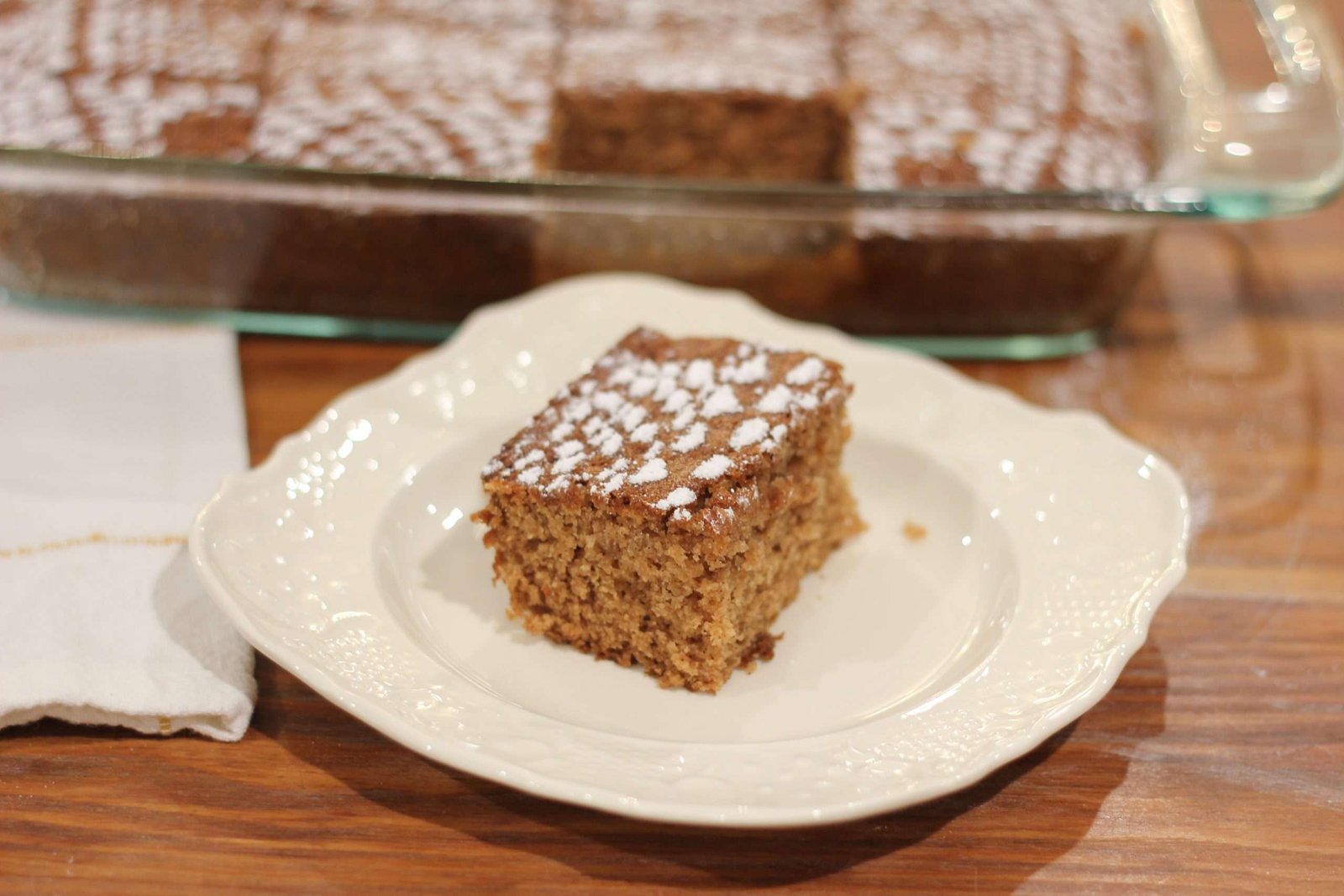 A slice of Applesauce Spice Cake on white plate with cake behind it.