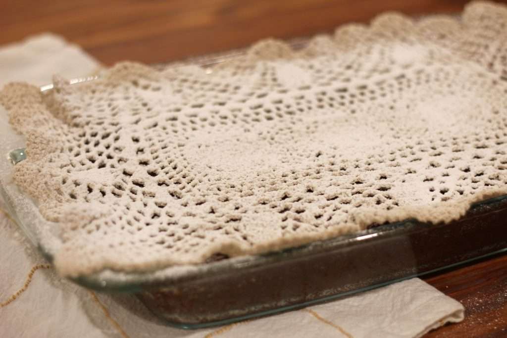 doily on top of baked applesauce cake with powdered sugar dusted on top.